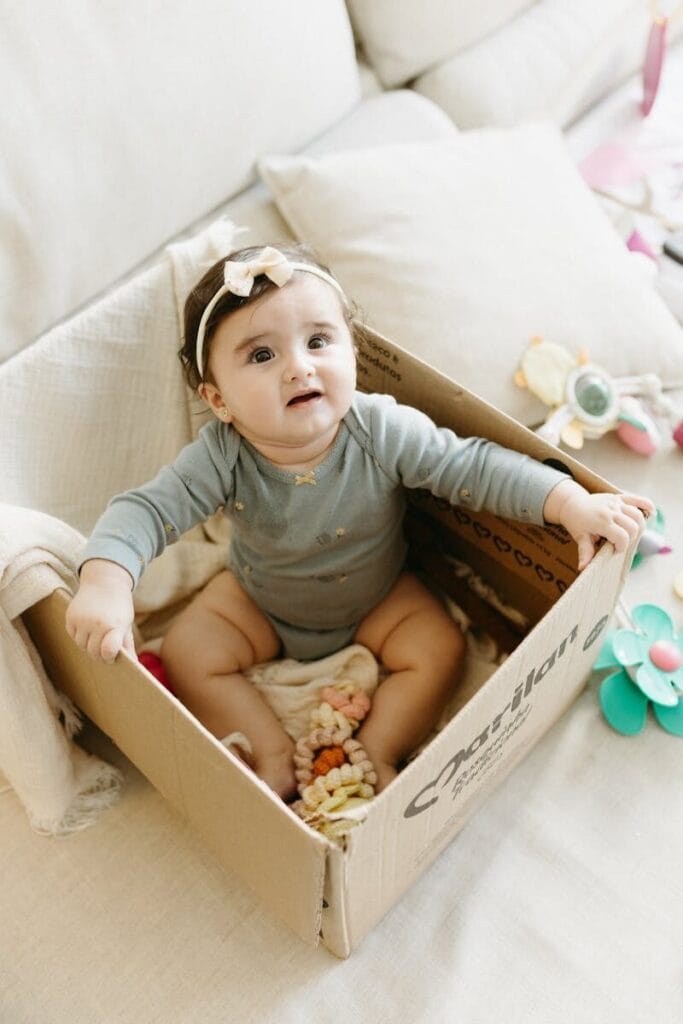Cute baby enjoying playtime inside a cardboard box surrounded by toys in a cozy room.
