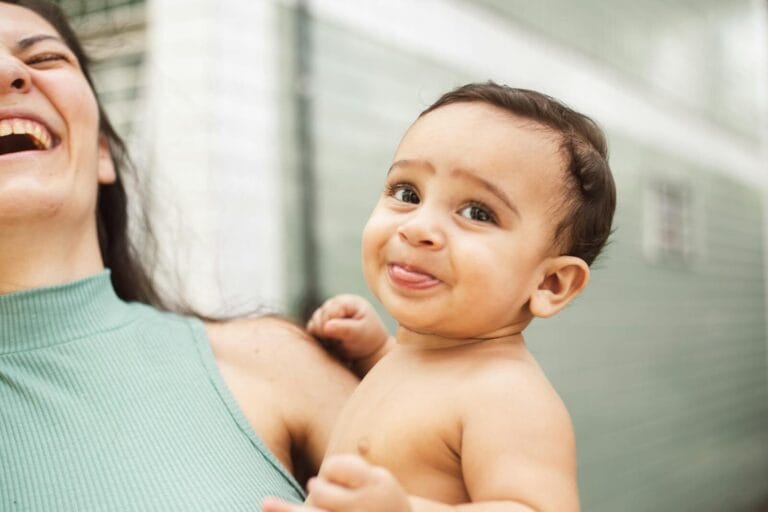 Heartwarming moment of a mother and baby sharing laughter indoors, capturing pure joy and affection.