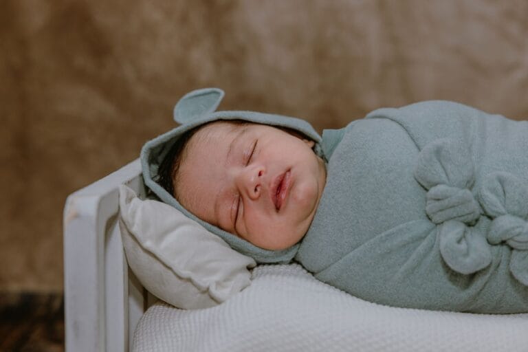 Adorable newborn baby peacefully sleeping in a soft green wrap on a small bed.